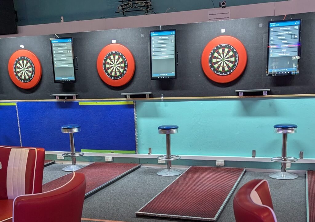 Ein Dartsalon mit vier elektrischen Dartscheiben, roten Sitzen und blauem Teppichboden.