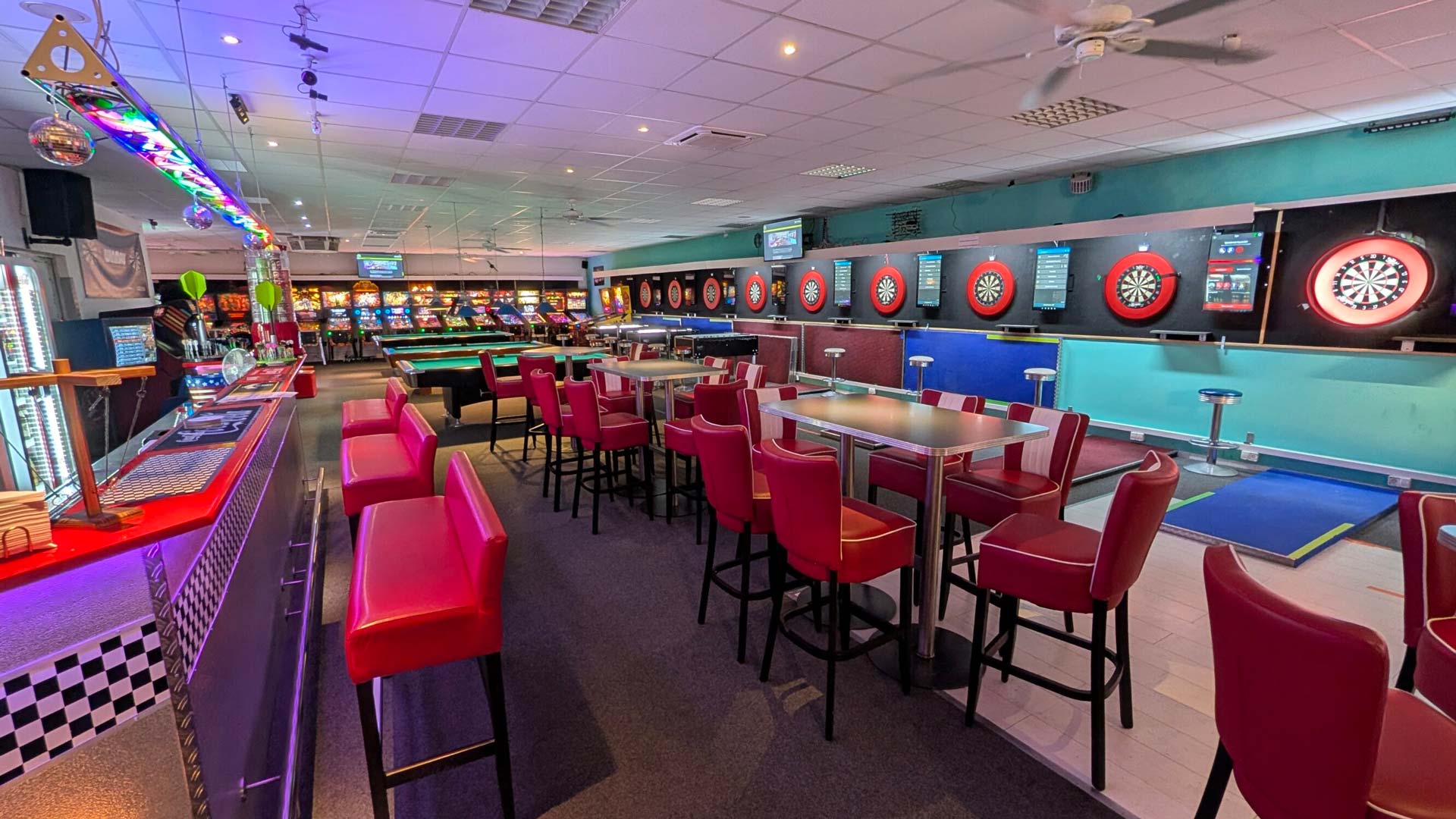 Blick in eine bunte Spielhalle mit roten Barhockern und mehreren Dartscheiben