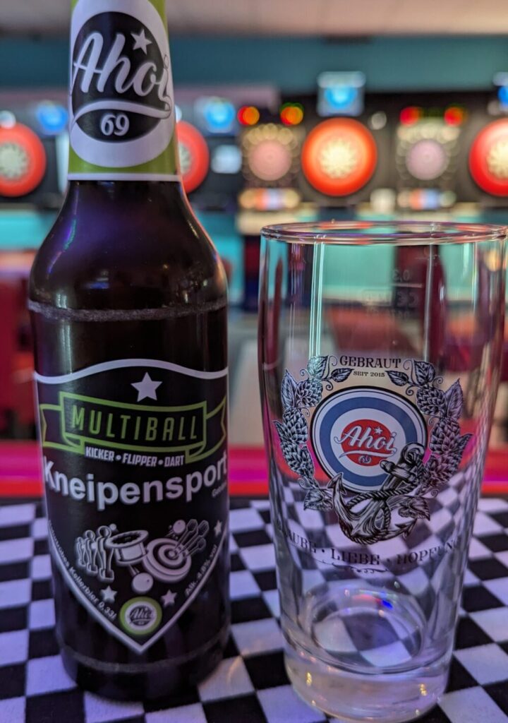 Bierflasche mit grünem Etikett und Ahoi Schriftzug steht neben einem verzierten Glas