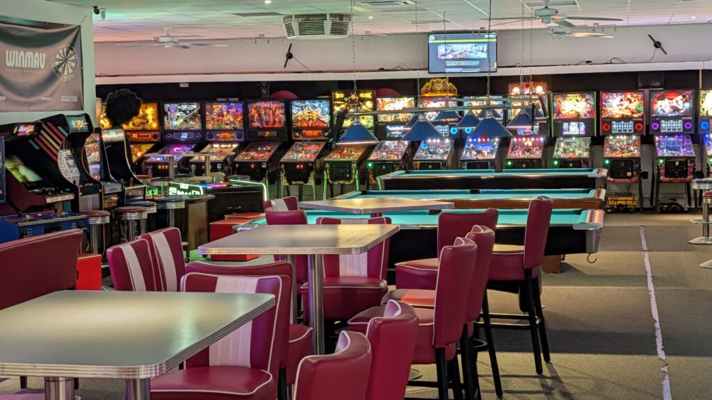 Leere Spielhalle mit bunten Flippern und pinken Stuehlen, nostalgisch