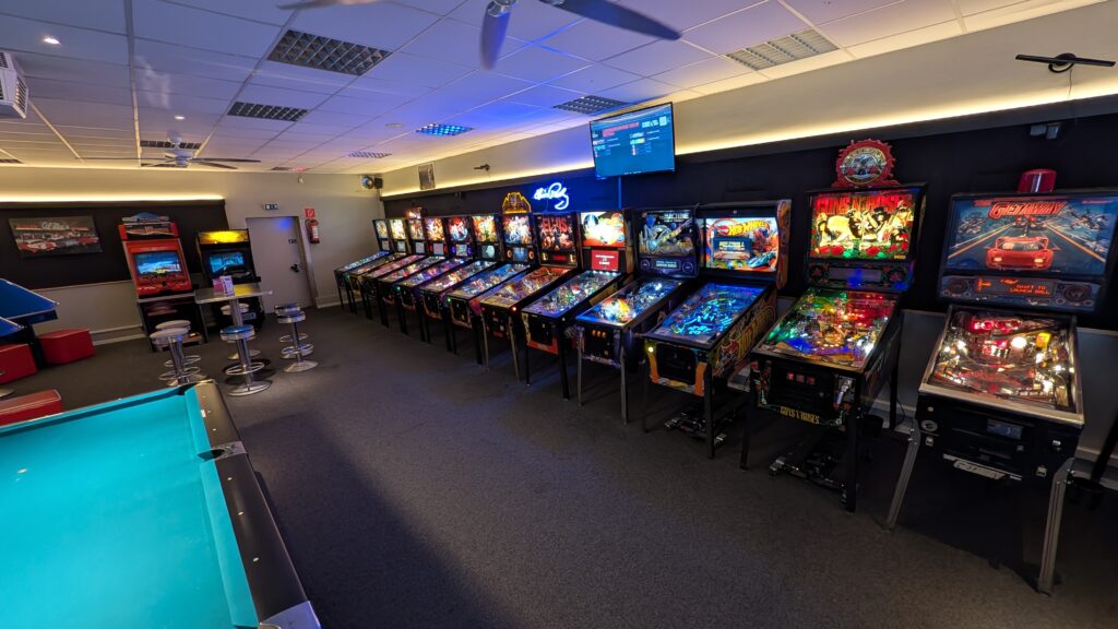 Spielhalle mit bunt leuchtenden Flipperautomaten und einem Billardtisch im Vordergrund