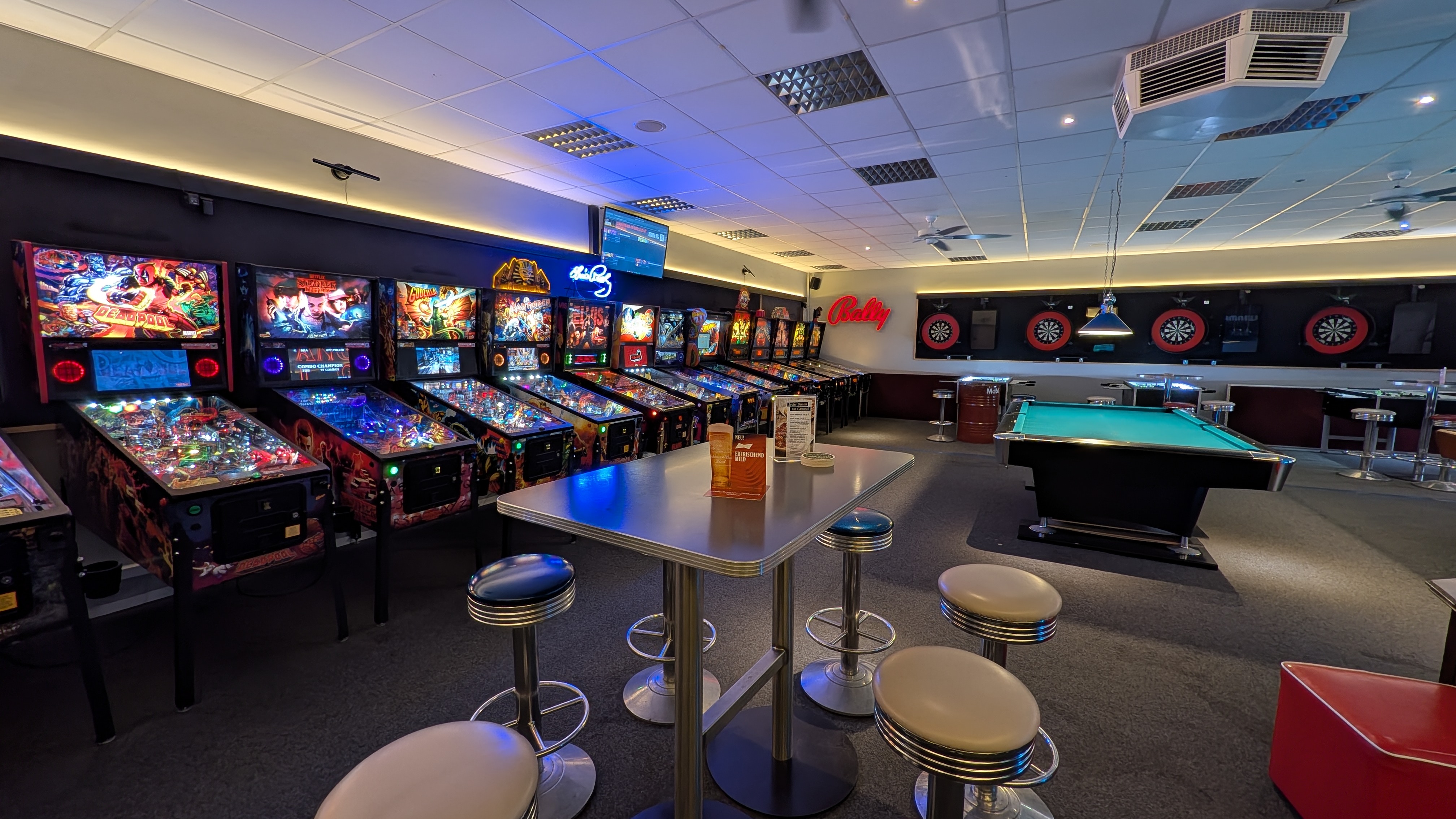 Spielhalle mit bunten Flipperautomaten Billardtisch Dartscheiben und Barhockern