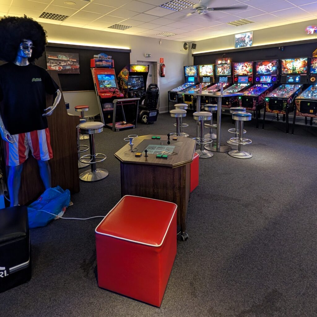 Retro Spielhalle mit bunten Flipperautomaten und einer Schaufensterpuppe mit Afroperuecke