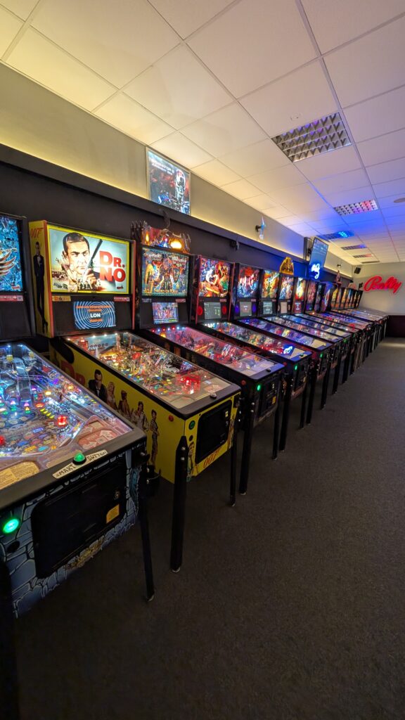Lange Reihe bunter Flipperautomaten in einer Spielhalle mit leuchtenden Displays