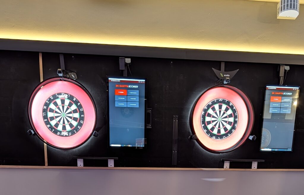 Zwei beleuchtete Dartscheiben mit Bildschirmen und Barhockern in einer Dartbar