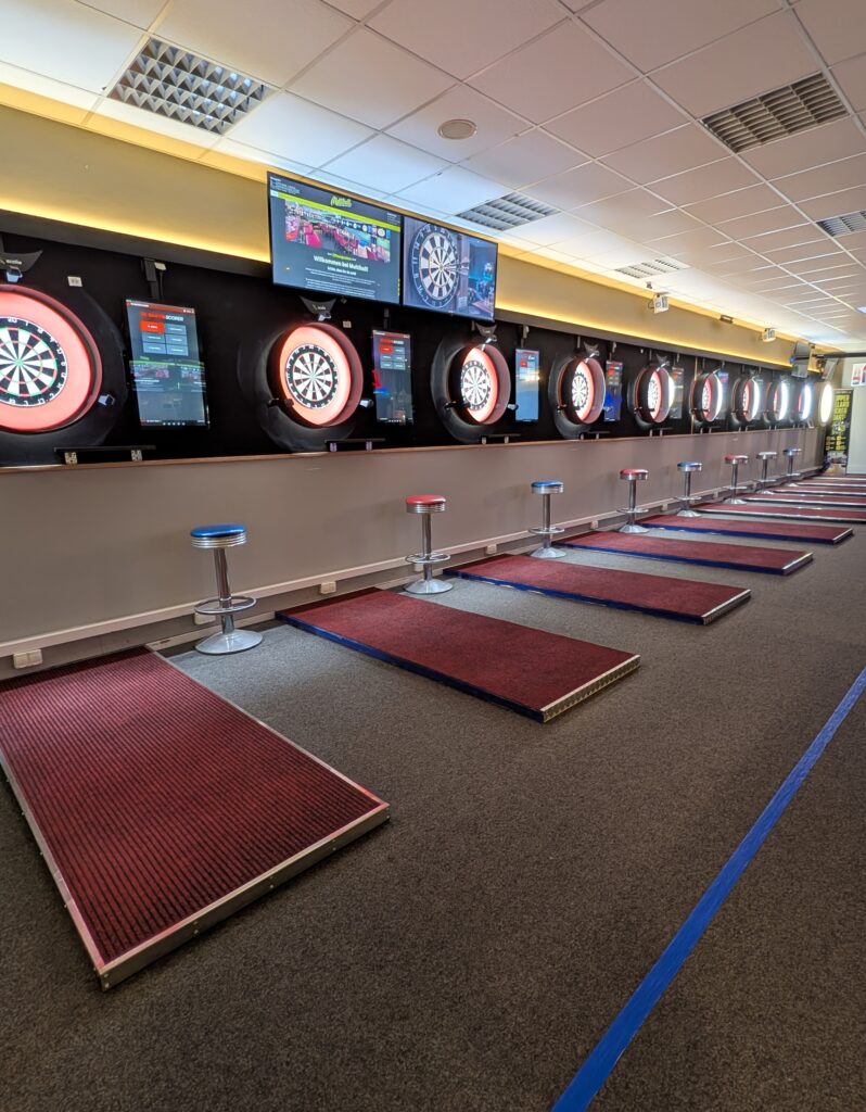Dartraum mit beleuchteten Dartscheiben roten Matten und Barhockern an der Wand