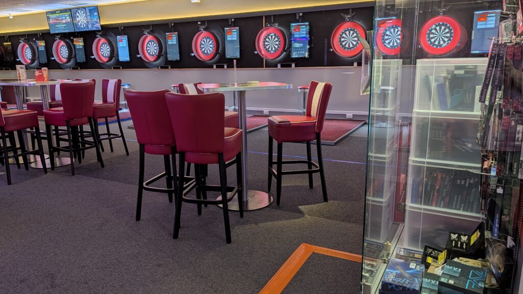 Dartlokal mit roten Barhockern und beleuchteten Dartscheiben an der Wand