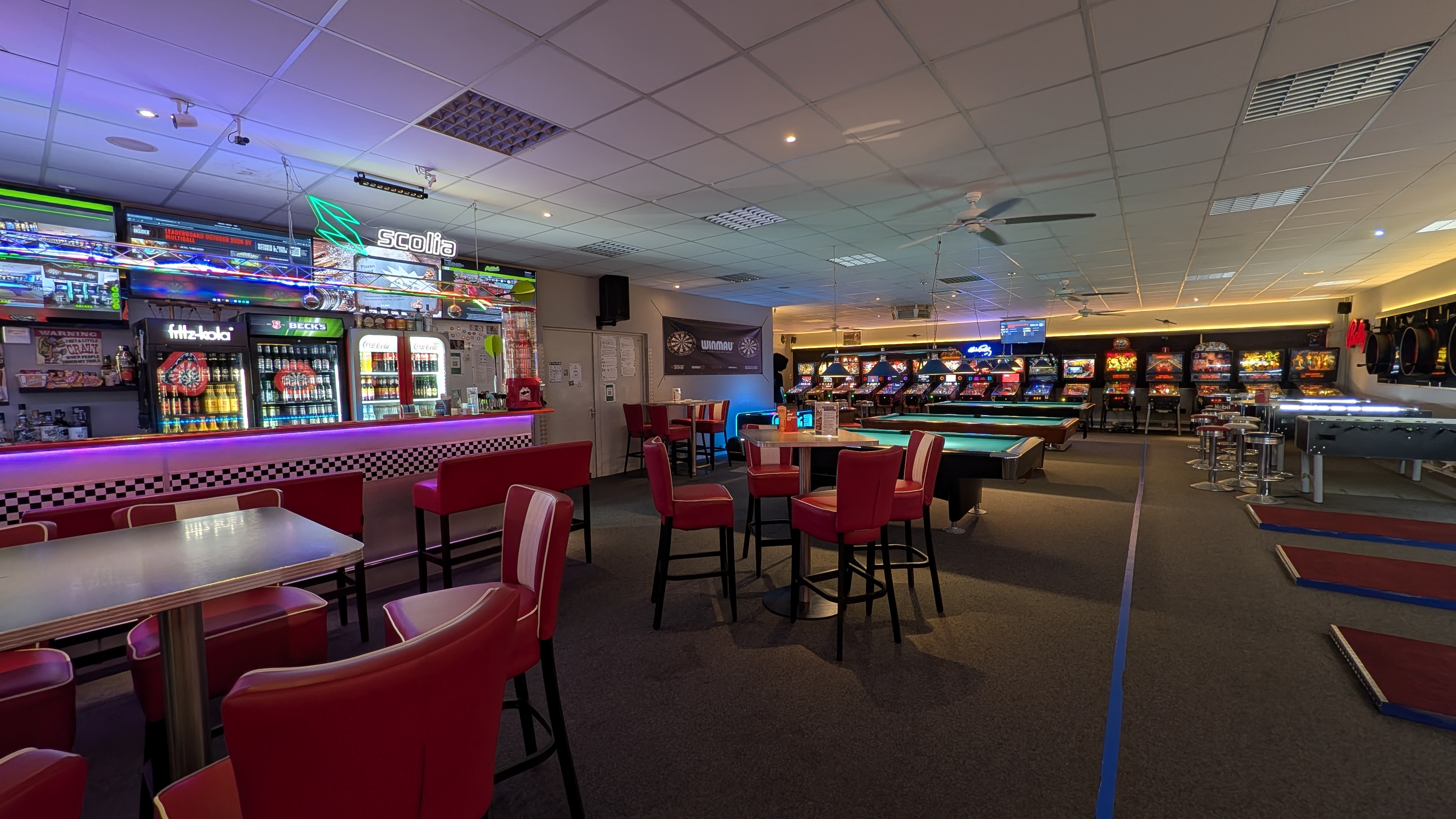 Bunte Spielhalle mit Billardtischen roten Barhockern und Flipperautomaten